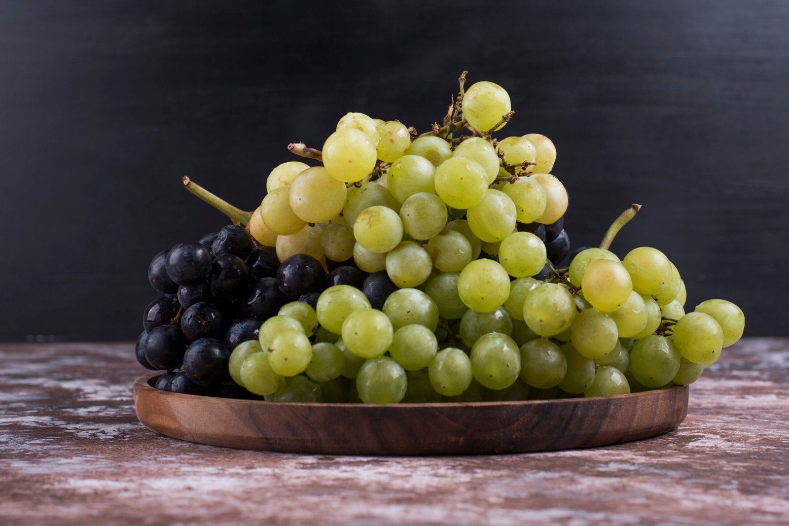 A bunch of green and red grapes in a wooden platter on black background. High quality photo